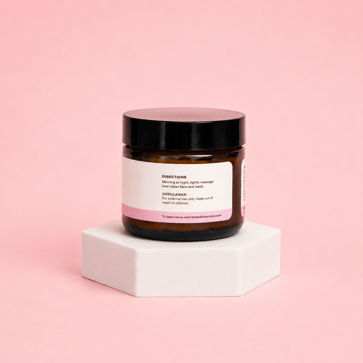 Jar of cream with a black lid on a white block against a pink background