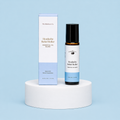 The Elderberry Co. Headache Relief Roller essential oil blend with its matching retail box displayed on a white pedestal against a soft blue background.